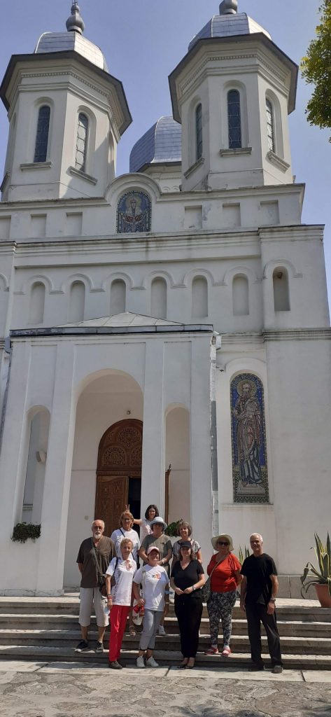 Picture of a church, that is white and has two towers. There are people standing in front of the church