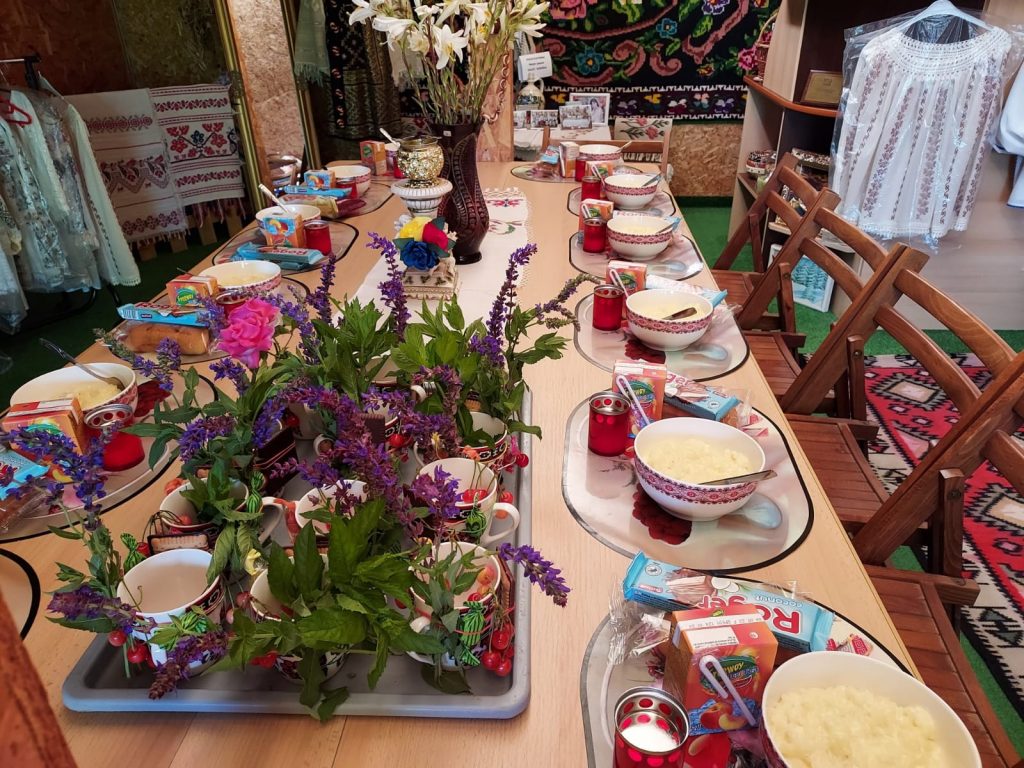 Picture of a decorated table. There sets of plates and food. Also red candles and colourful flowers standing on the table
