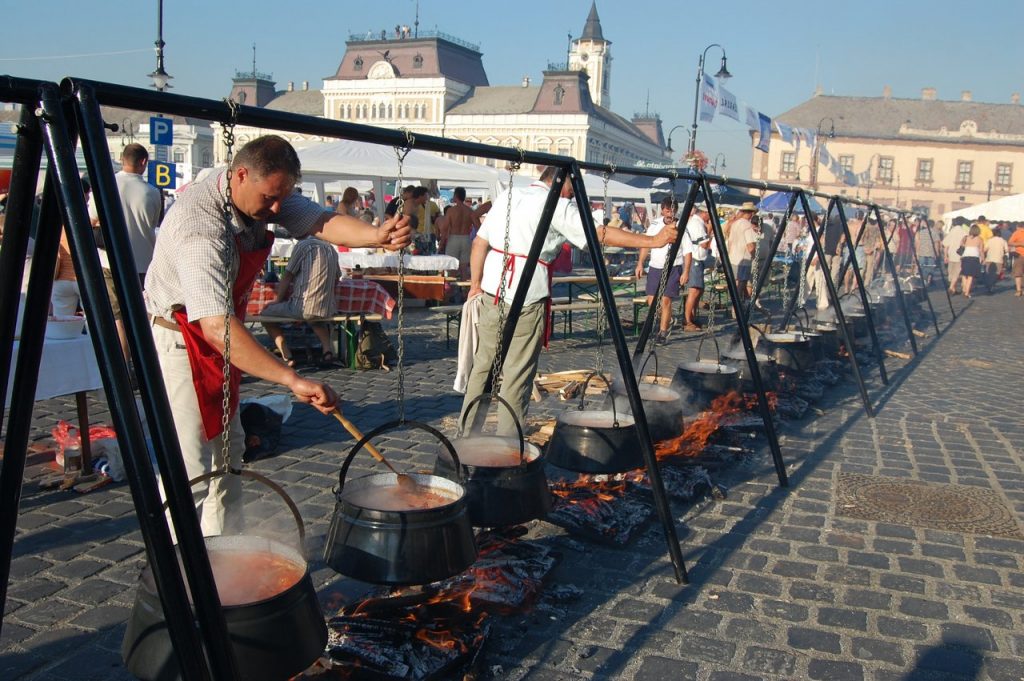A photo of the festival showing a row of steaming kettles filled with fish soup, with people cooking around them
